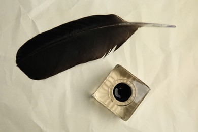 Photo of Feather pen and inkwell on old crumpled paper, flat lay