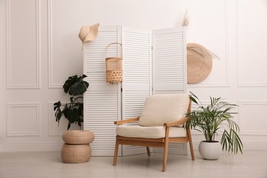 Photo of Stylish photo zone with white folding screen, plants and comfortable armchair indoors