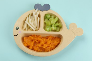 Photo of Healthy baby food. Section plate with delicious pumpkin puree and vegetables on light blue background, top view