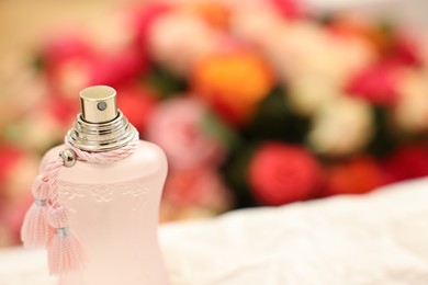 Bottle of perfume on crumpled paper against beautiful roses, closeup. Space for text