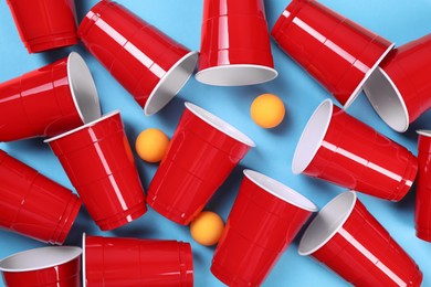 Photo of Plastic cups and balls for beer pong on light blue background, flat lay