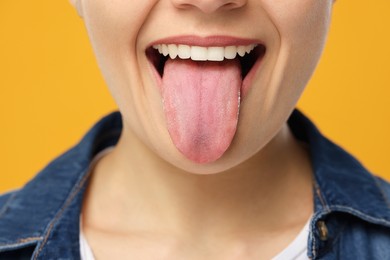 Photo of Happy young woman showing her tongue on yellow background, closeup
