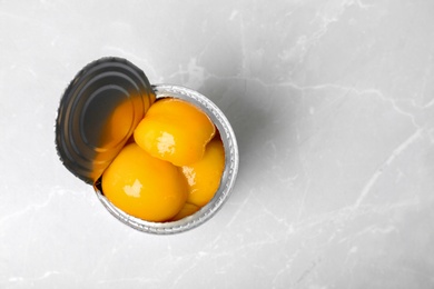 Photo of Tin can with conserved peaches on light background, top view
