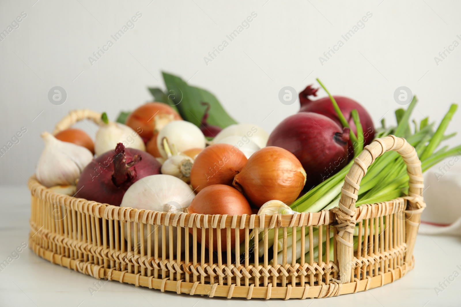 Photo of Wicker tray with fresh onions and garlic on white table