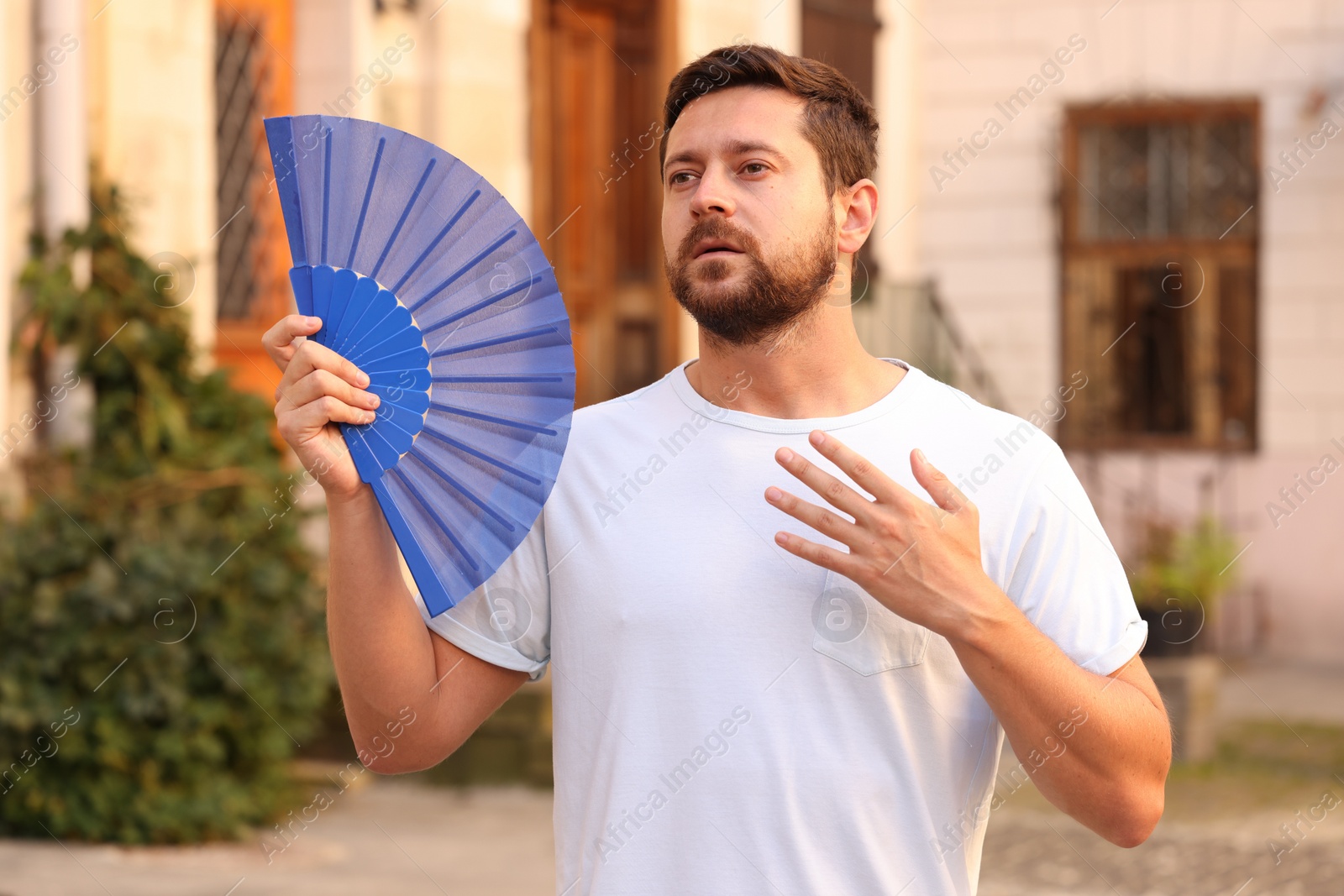 Photo of Man with hand fan suffering from heat outdoors