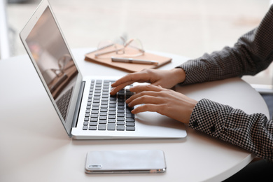 Photo of Young blogger working with laptop at table indoors, closeup