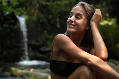 Photo of Beautiful young woman in stylish bikini relaxing near mountain waterfall outdoors. Space for text