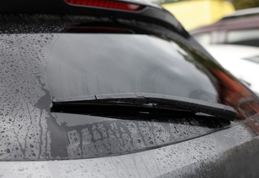 Car wiper cleaning water drops from rear windshield glass outdoors, closeup