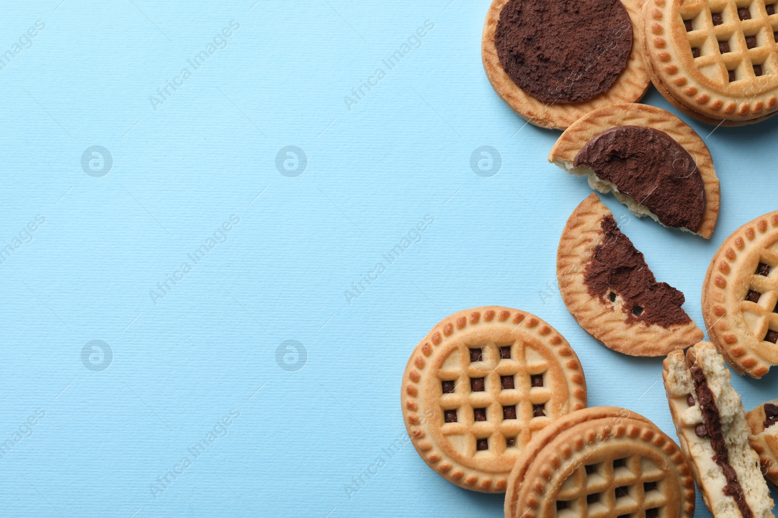 Photo of Tasty sandwich cookies with cream on light blue background, flat lay. Space for text
