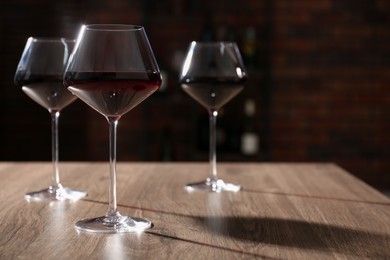 Photo of Tasty red wine in glasses on wooden table, space for text