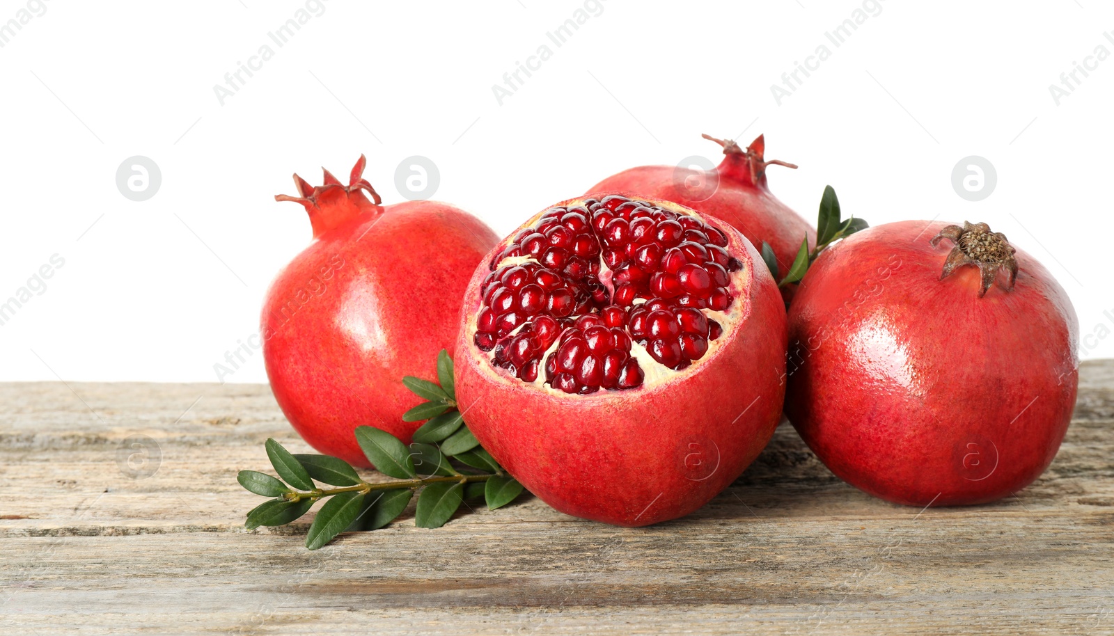 Photo of Fresh pomegranates and green leaves on wooden table against white background