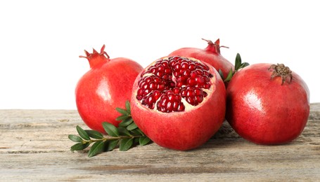 Fresh pomegranates and green leaves on wooden table against white background