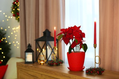 Photo of Potted poinsettia, burning candles and festive decor on dresser in room, space for text. Christmas traditional flower