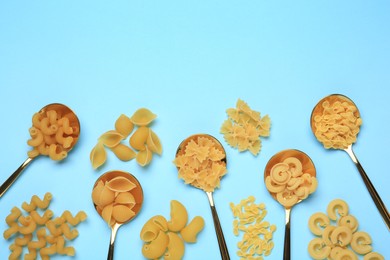 Photo of Spoons with different types of pasta on light blue background, flat lay. Space for text