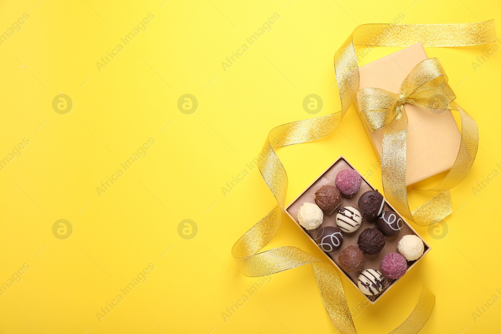 Open box with delicious chocolate candies and ribbon on yellow background, top view. Space for text Photo of Open box with delicious chocolate candies and ribbon on yellow background, top view. Space for text