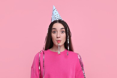 Photo of Woman in party hat with blower and streamers on pink background