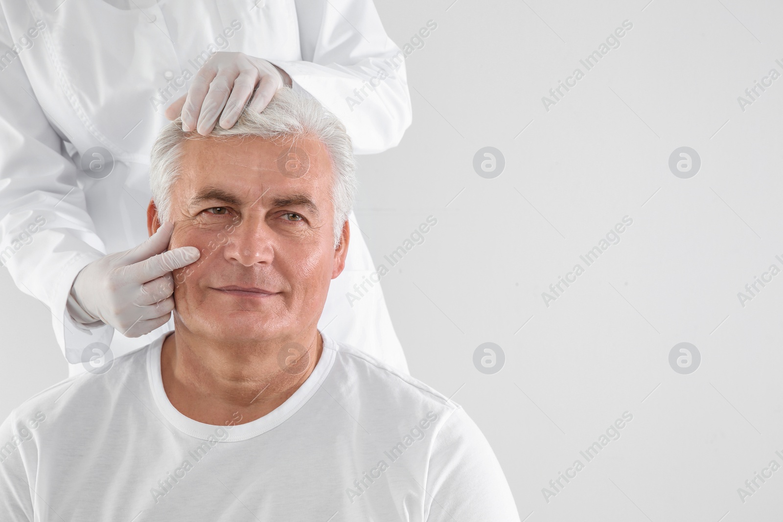 Photo of Doctor examining senior man face before cosmetic surgery on white background. Space for text