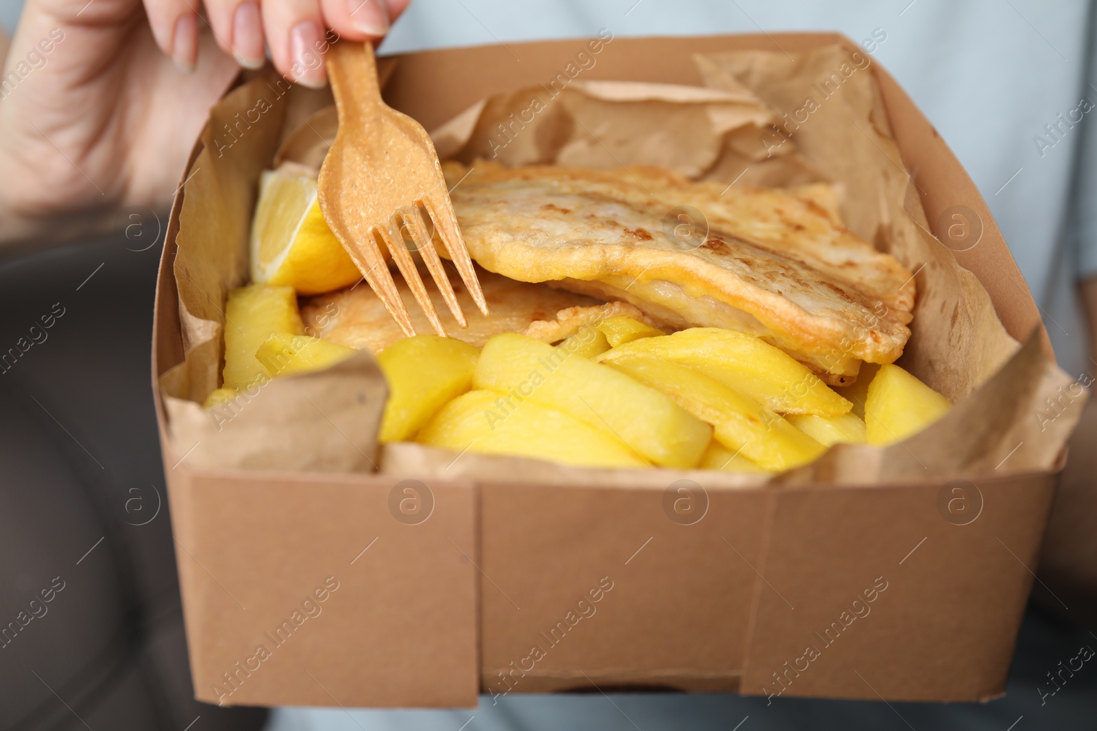 Photo of Woman eating delicious fish and chips on gray background, closeup