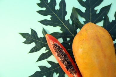 Photo of Whole and cut fresh ripe papaya fruits with leaf on light green background, flat lay. Space for text