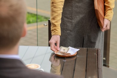 Photo of Waitress taking tips from wooden table in outdoor cafe, closeup