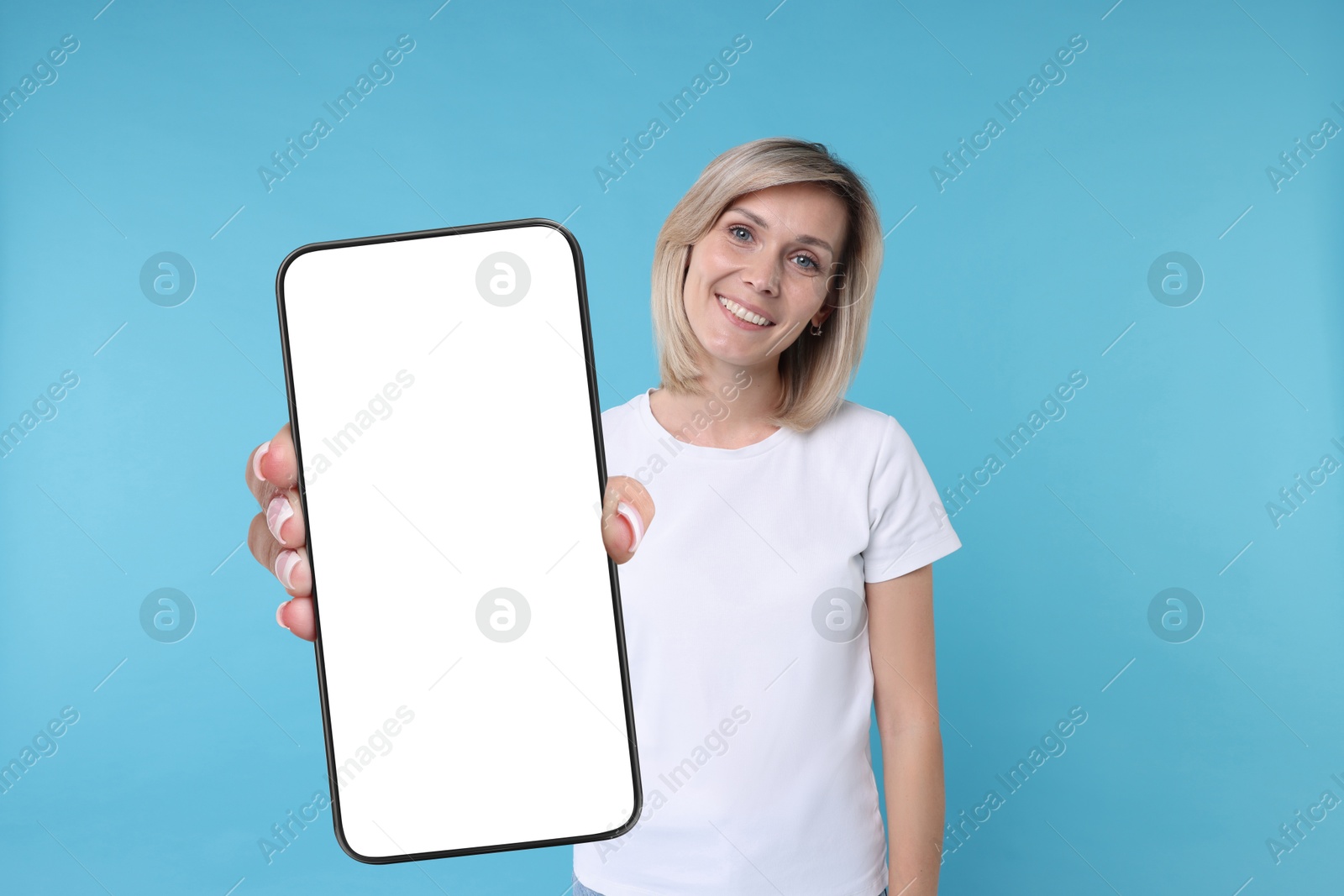 Image of Happy woman showing mobile phone with blank screen on light blue background. Mockup for design