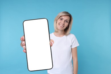 Happy woman showing mobile phone with blank screen on light blue background. Mockup for design