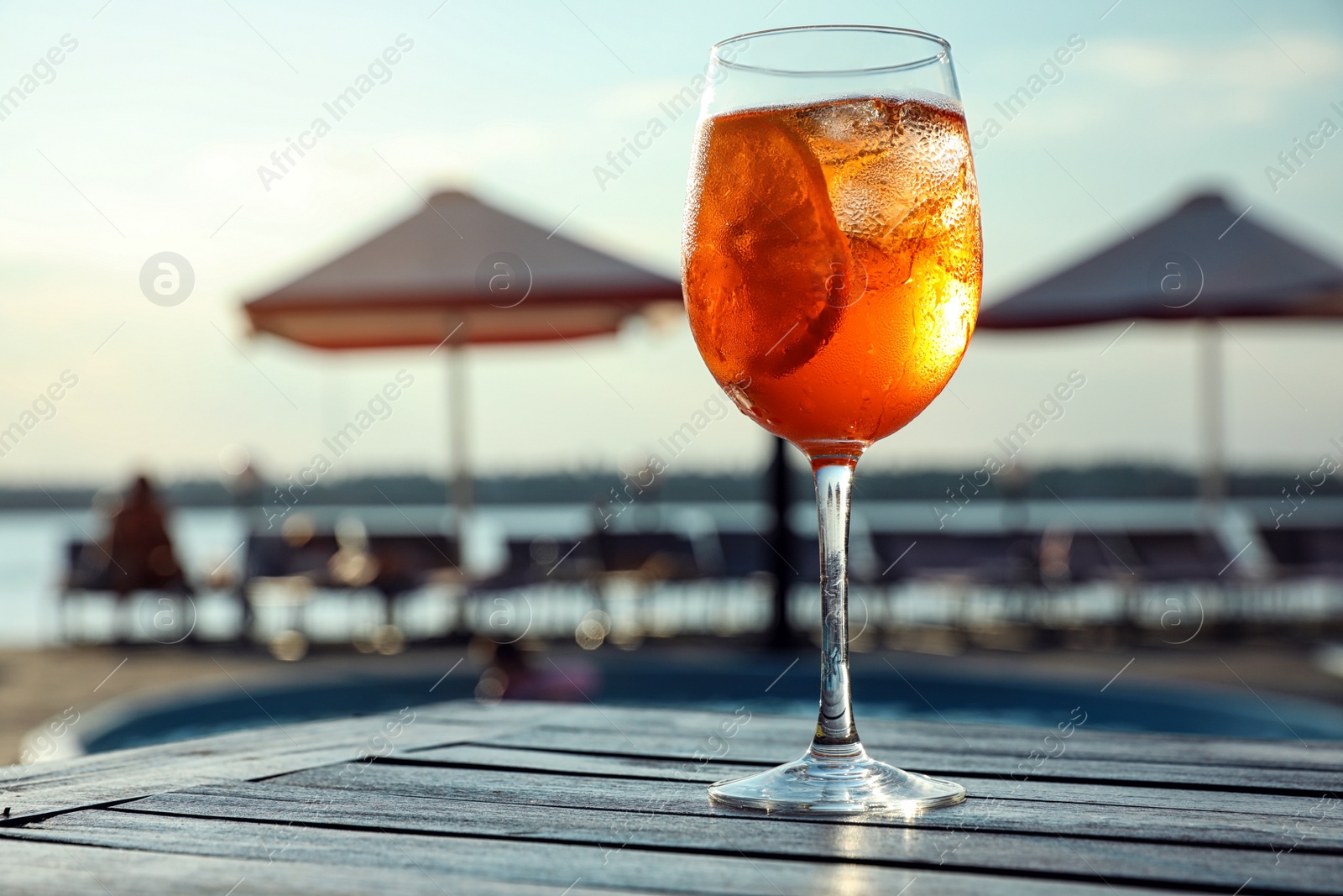 Photo of Glass of fresh summer cocktail on wooden table near swimming pool outdoors. Space for text