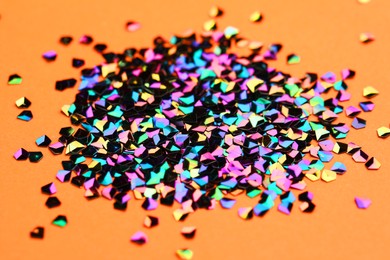 Photo of Pile of shiny glitter on orange background, closeup