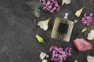 Bottle of luxury perfume and floral decor on dark grey table, flat lay. Space for text