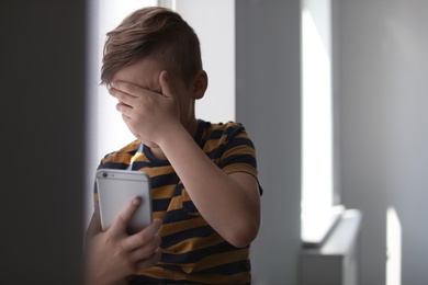 Photo of Frightened little child with smartphone indoors. Danger of internet