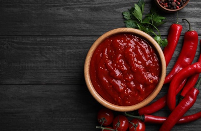 Flat lay composition with bowl of chili sauce and ingredients on wooden table. Space for text