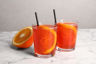 Photo of Aperol spritz cocktail, orange slices and straws in glasses on white marble table