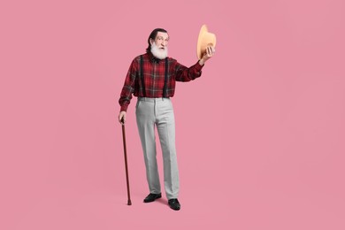 Senior man with hat and walking cane on pink background