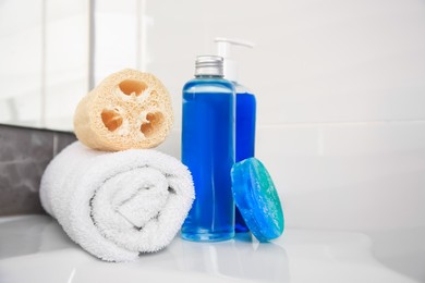Photo of Loofah sponge, rolled towel and cosmetic products on sink in bathroom