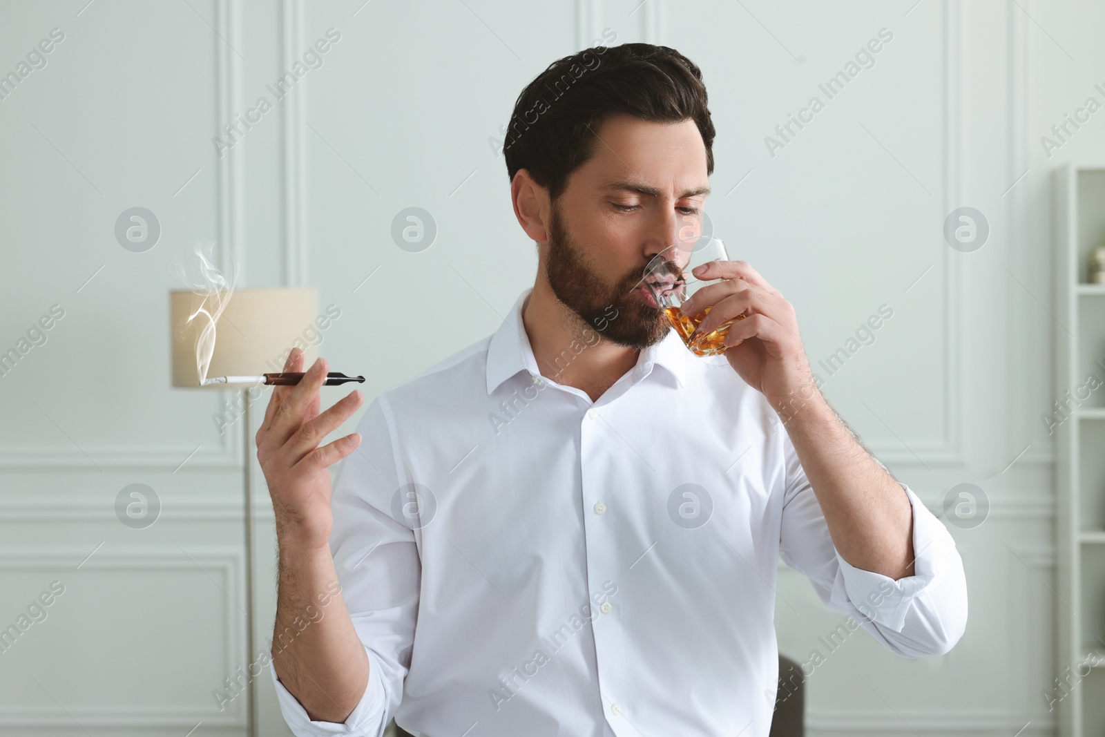 Photo of Man using cigarette holder for smoking and drinking whiskey in office