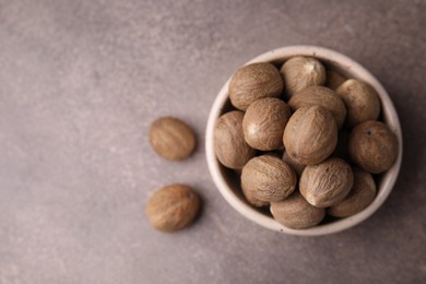 Whole nutmegs in bowl on brown table, top view. Space for text