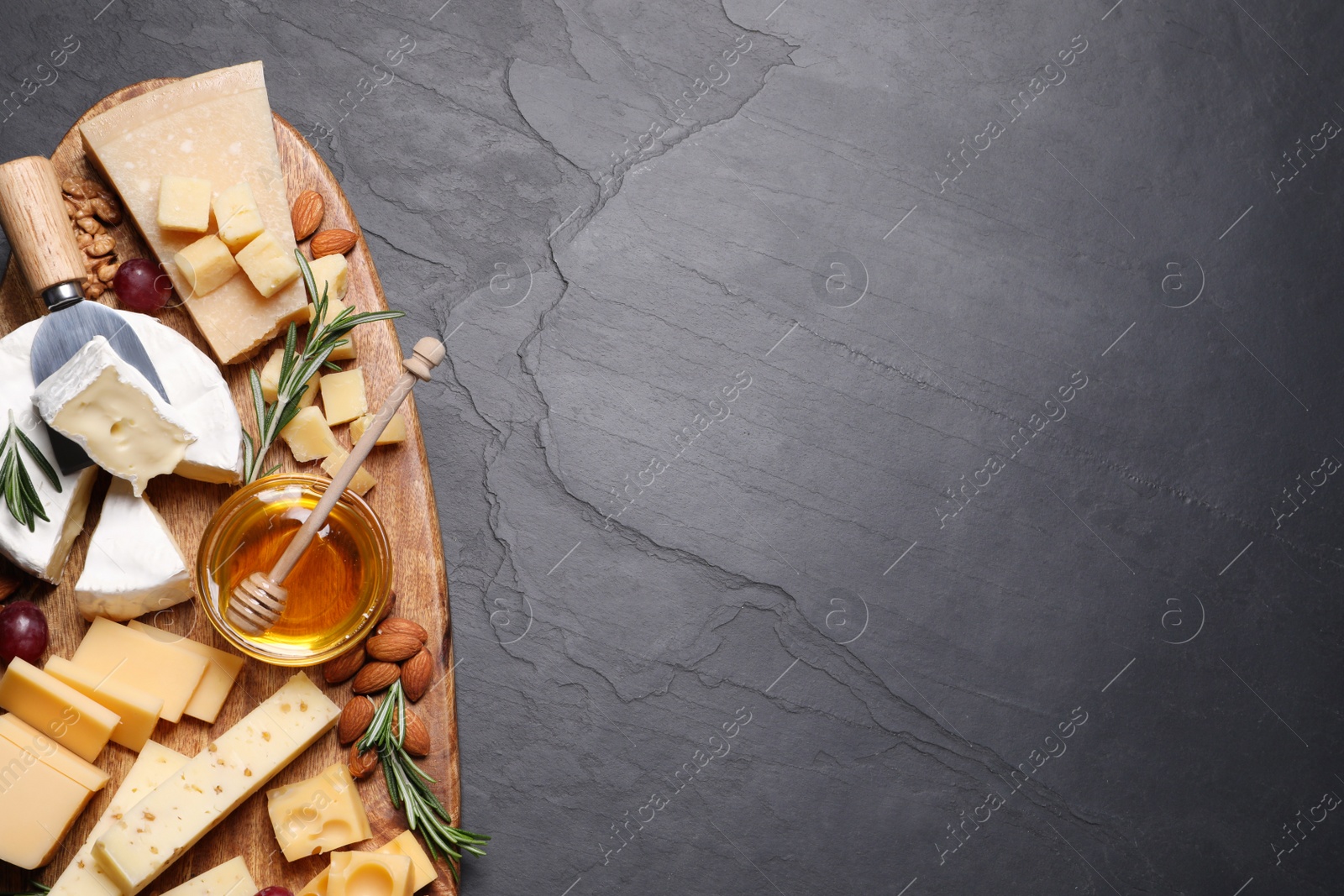 Photo of Cheese plate with honey, grapes and nuts on black table, top view. Space for text