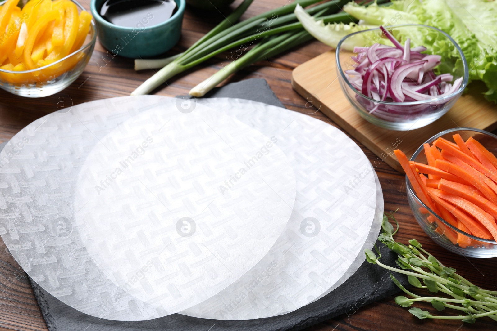 Photo of Rice paper, microgreens and other ingredients for spring rolls on wooden table, closeup