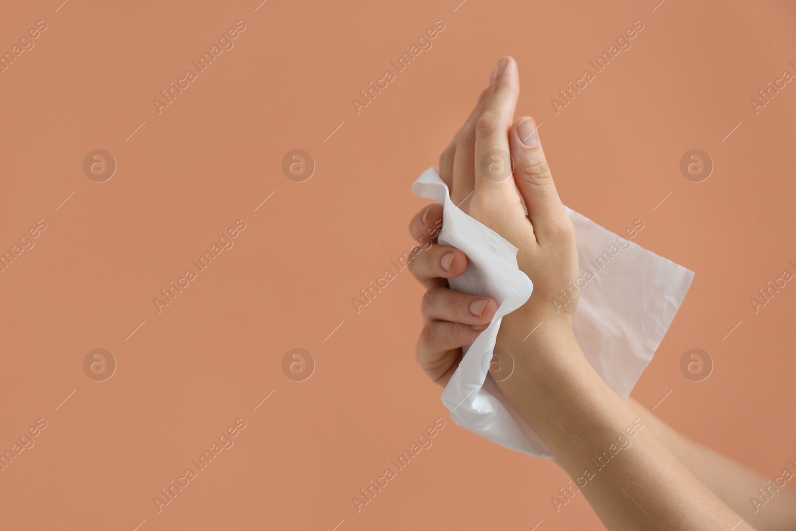 Photo of Woman cleaning hands with paper tissue on light brown background, closeup. Space for text