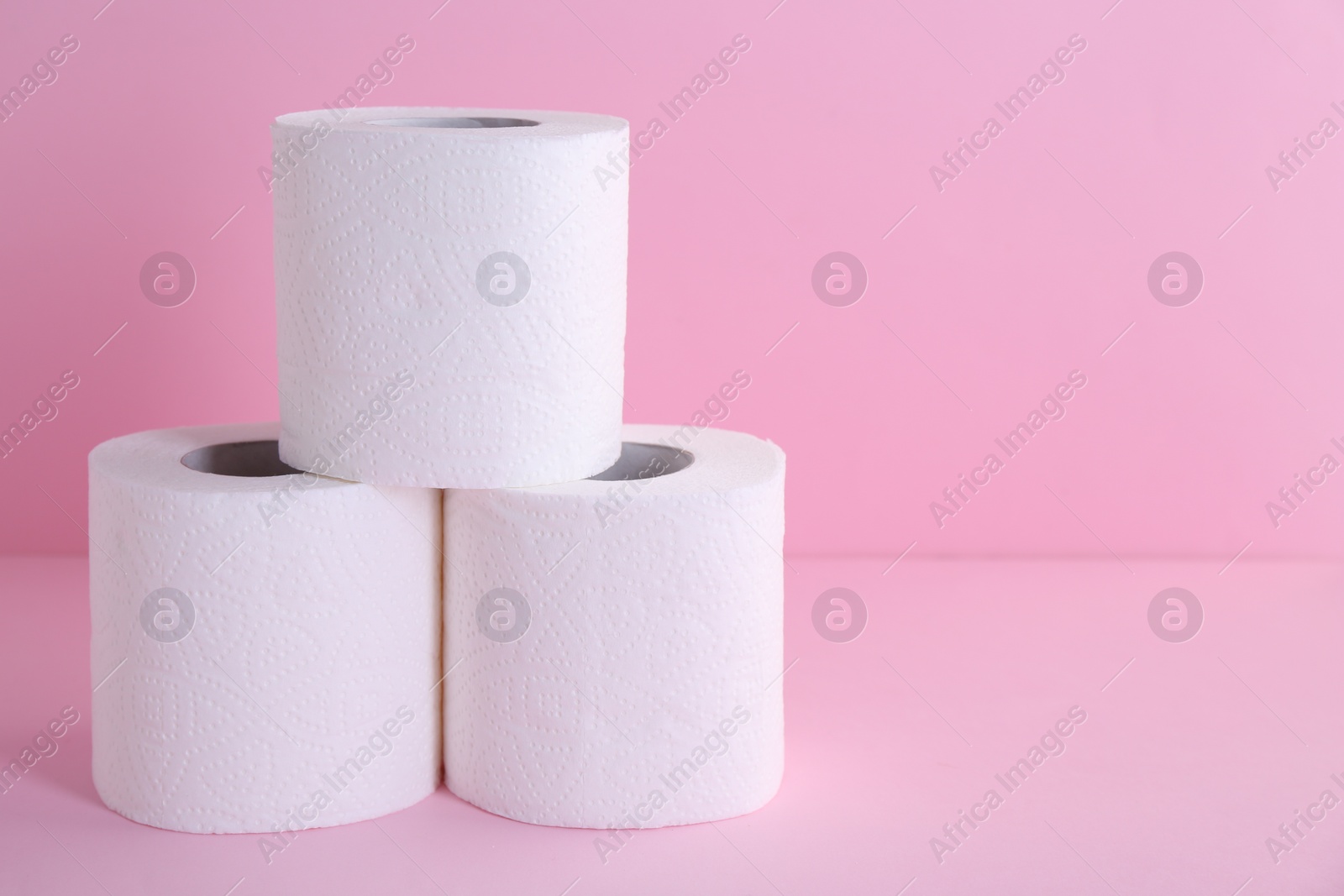 Photo of Soft toilet paper rolls on pink background, closeup. Space for text