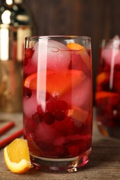 Photo of Tasty cranberry cocktail with ice cubes and orange in glass on wooden table