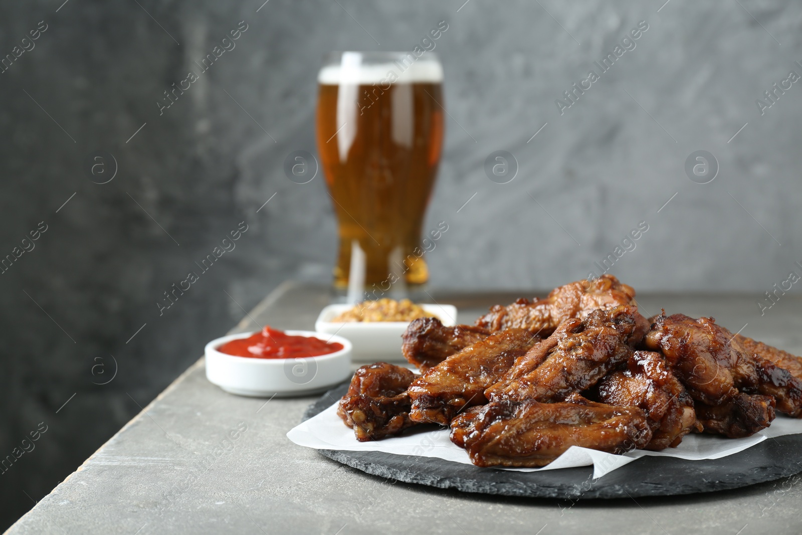 Photo of Delicious chicken wings served with beer on grey table. Space for text