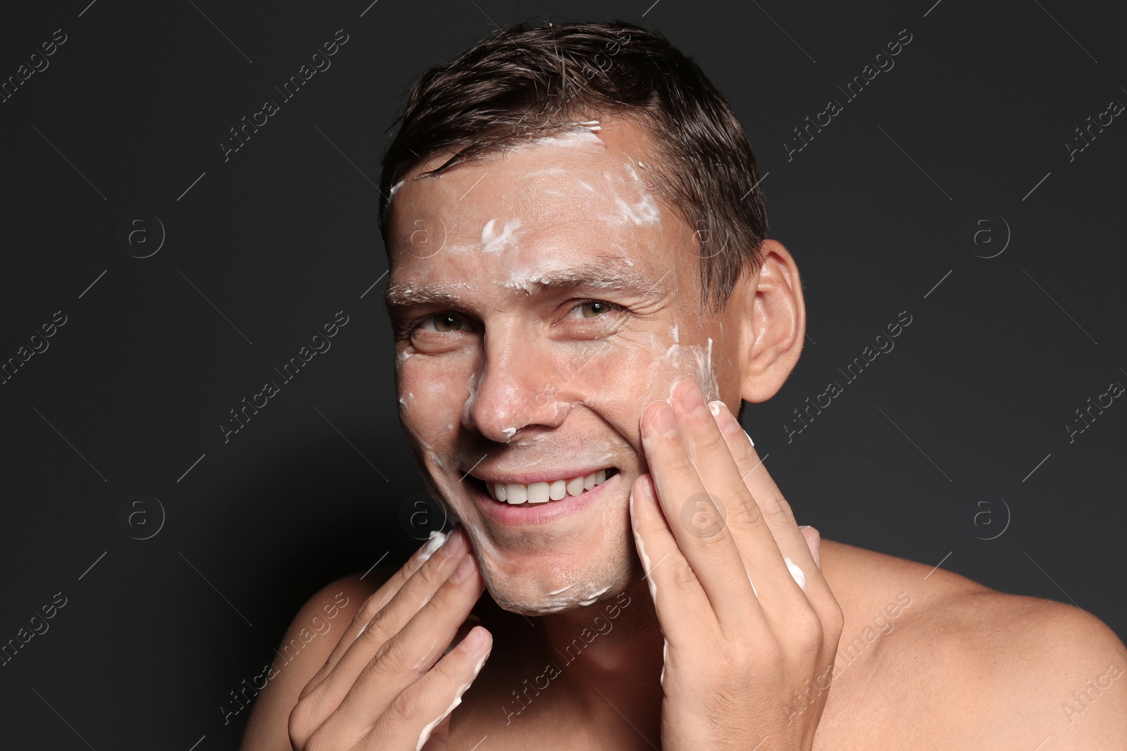 Photo of Man washing face with soap on dark background