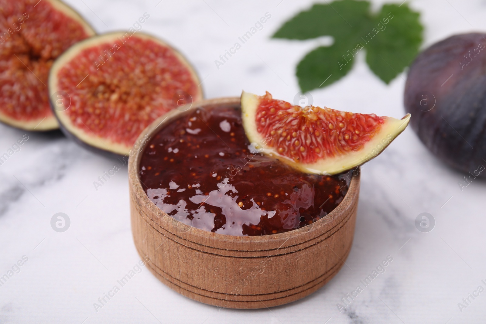 Photo of Bowl of tasty sweet fig jam and fruits on white marble table, closeup