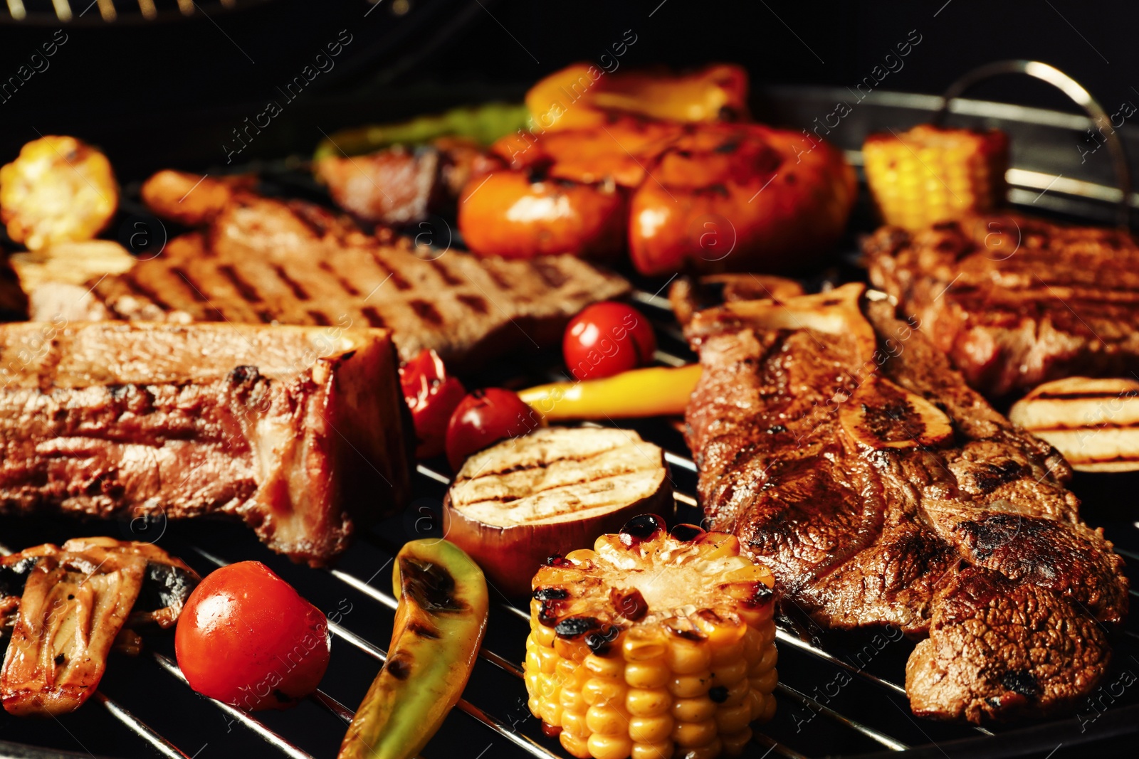 Photo of Fresh grilled meat steaks and vegetables on barbecue grate, closeup