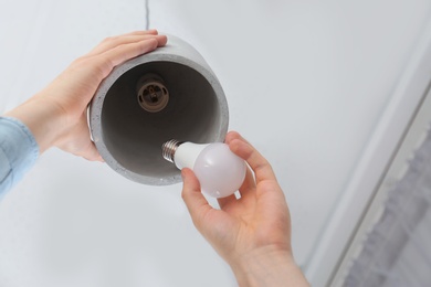 Man changing light bulb in pendant lamp indoors, closeup. Low angle view