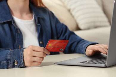 Woman with credit card using laptop at white table indoors, closeup