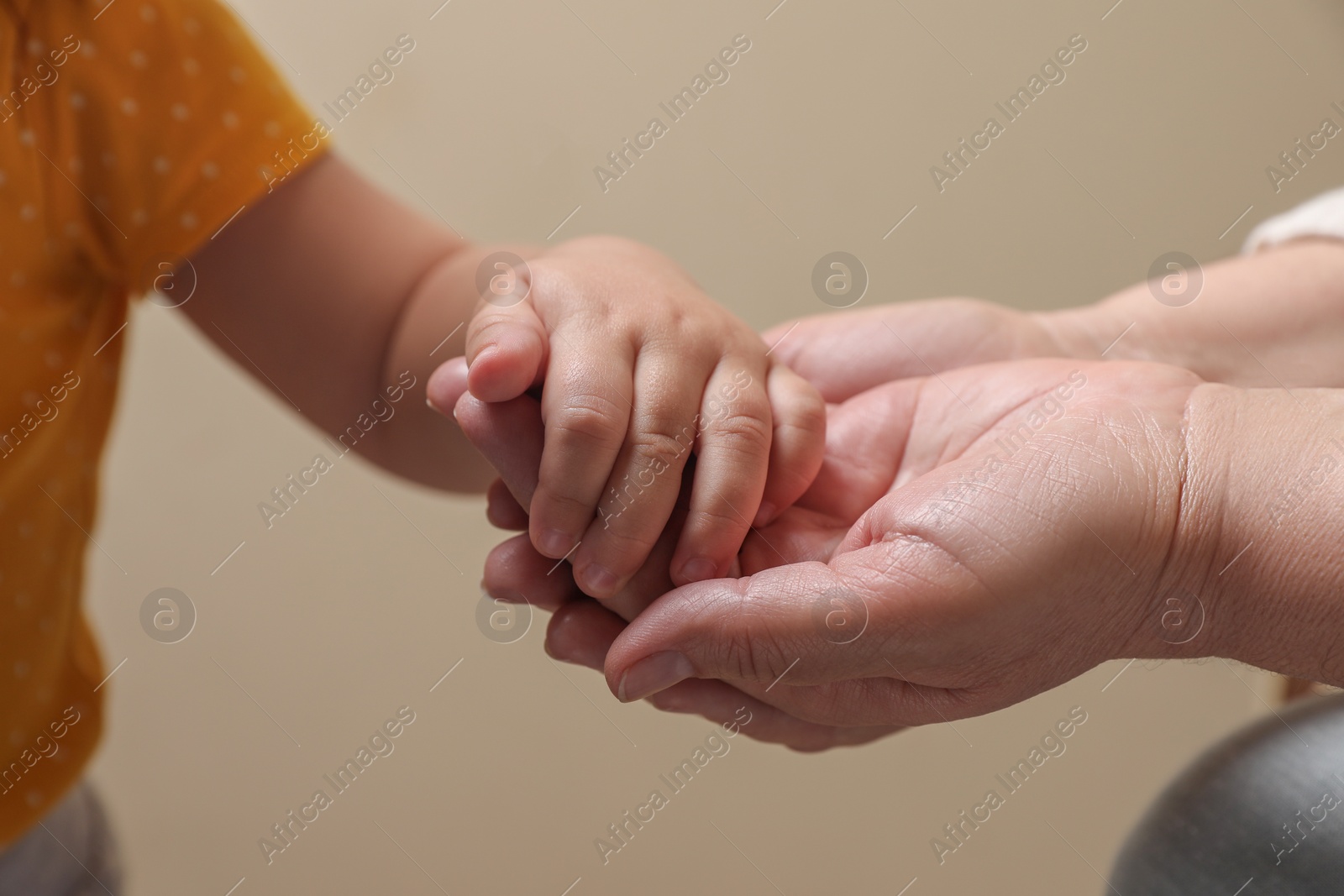 Photo of Woman holding hands with her granddaughter on beige background, closeup