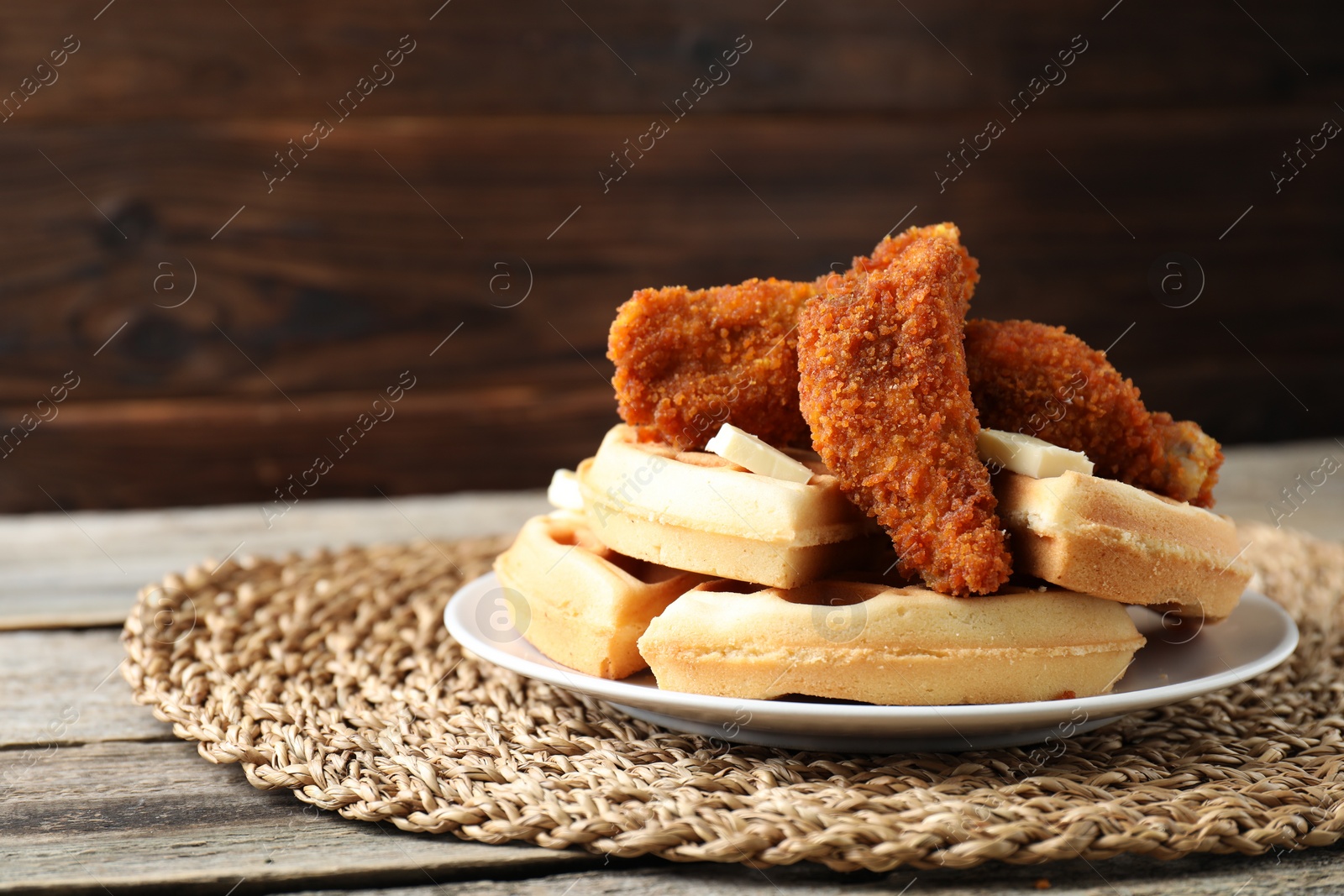 Photo of Delicious Belgium waffles served with fried chicken and butter on wooden table, closeup. Space for text