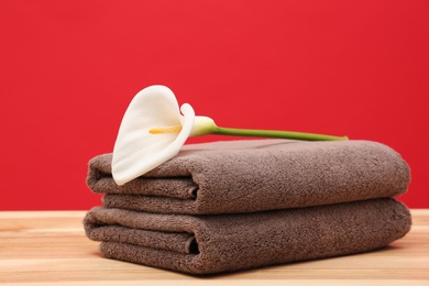 Soft clean towels with beautiful flower on table against color background